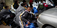 Mehrere Flüchtlinge sitzen auf dem Boden und tragen Wärmedecken