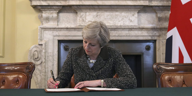 Eine Frau sitzt an einem Tisch und unterzeichnet etwas