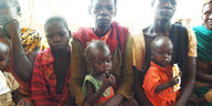 Drei Frauen mit ihren Kindern sitzen auf einer Bank vor dem Saint Mary's Hospital in einem Dorf im Südsudan und warten auf Hilfe.