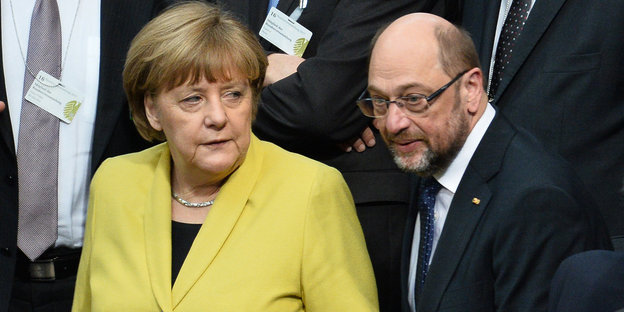 Angela Merkel im zitronengelben Blazer, neben ihr im schwarzen Anzug und leicht nach vorne gebeugt, ihr Herausforderer Martin Schulz