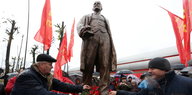 In Weißrussland legen Männer rote Nelken an einem Lenindenkmal nieder