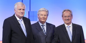 Drei Männer in Anzügen in einem Fernsehstudio
