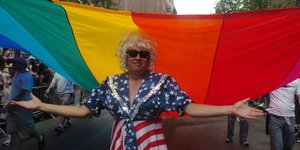 Eine Person in US-Farben gekleidet unter einer Regenbogenflagge