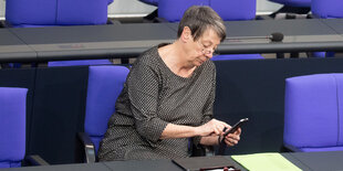 Eine Frau in mit kurzen Haaren sitzt auf einem blauen Stuhl und guckt auf ihr Handy