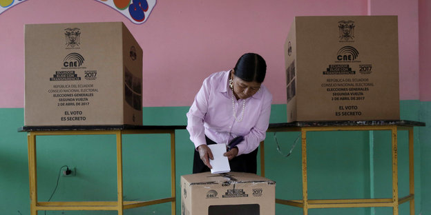 Eine Frau steckt einen Zettel in einer Wahlurne aus Pappe