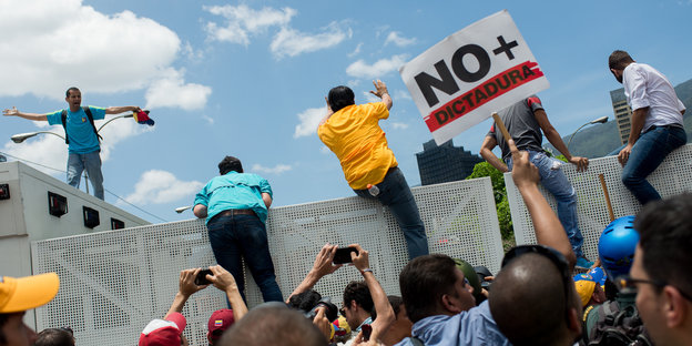 Demonstranten in bunten Shirts klettern auf einer Mauer herum