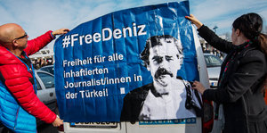 Zwei Menschen halten ein #FreeDeniz-Plakat hoch