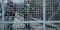 Im Vordergrund Zaun mit Stacheldraht, im Hintergrund Soldaten