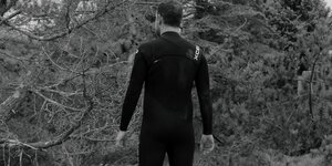 S/W-Foto: Rückenansicht von dunkelgekleidetem Mann vor Bäumen