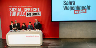 Fünf Menschen an einem Pult neben einem Bildschirm, auf dem „Sahra Wagenknecht, Die Linke“ steht