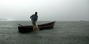 Ein Fischer zieht, im Boot stehend, sein Netz ein
