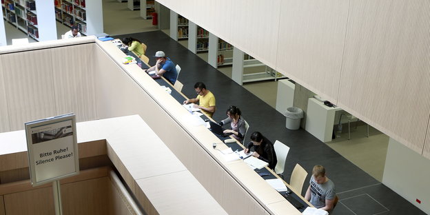 Menschen an einer längeren Reihe Arbeitsplätze in einer Bibliothek