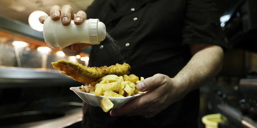 Koch streut Salz auf eine Portion Fish and Chips