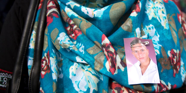 Ein blaues Kopftuch mit verschiedenen Mustern, an das ein Porträtfoto eines jungen Mannes gesteckt ist