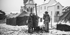 Ein schwarz-weiß Foto zeigt eine Gruppe Soldaten, im Hintergrund zwei Zelte und Häuser eines Dorfs