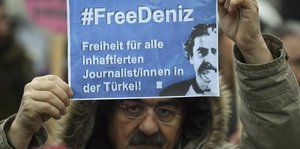 Ein Mensch hält ein Din A4-Blatt mit der Aufschrift: „#FreeDeniz. Freiheit für alle inhaftierten Journalist/innen in der Türkei“