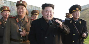 Kim Jong Un hat ein Fernglas in der Hand und blickt in die gleiche Richtung, wie die vier Uniform tragenden Männer hinter ihm