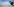 Ein Mann hat einen Golfschläger in der Hand und ist auf einem Rasen in der Hocke. Er guckt einen Golfball links im Bild an, im Hintergrund ein See