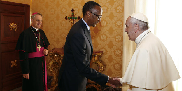 Rechts im Bild ein alter Mann in Papst-Kleidung, in der Mitte ein Mann in Anzug, der ihm die Hand gibt, ganz links im Bild ein Mann in Kardinals-Kleidung, der lacht