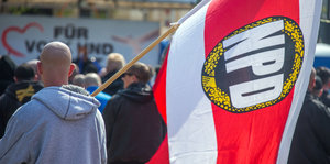 Ein Mann mit Glatze trägt eine NPD-Fahne über der Schulter