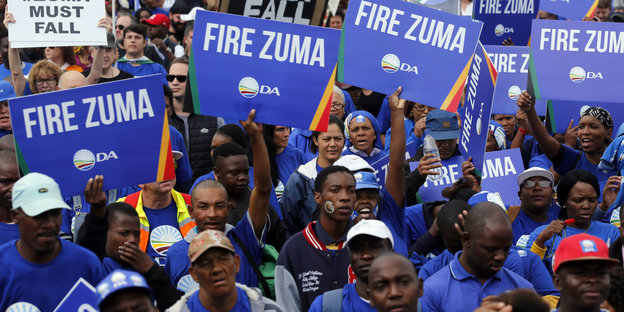 Menschen in blauen Shirts halten blaue Schilder hoch - Fire Zuma steht darauf