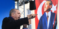 Erdogan brüllt in ein Mikrofon und zeigt mit ausgestrecktem Arm nach rechts, während Atatürk auf einer Fahne hinter ihm nach links blickt