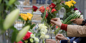 Hände, die Blumen an einen Zaun stecken