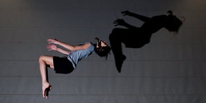 Eine Frau macht einen Rückwärtssalto, etwas versetzt sieht man ihren Schatten an der Wand