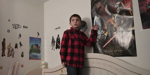 Junge steht auf einem Bett, an der Wand Star-Wars-Poster