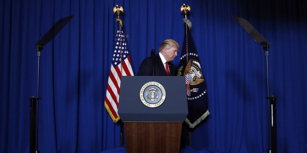 Trump dreht sich hinter einem Rednerpult zur Seite