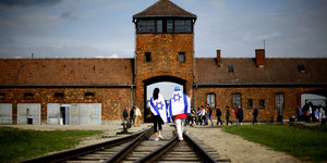 Zwei junge Leute mit Israel-Flaggen laufen über die Gleise zum Tor von Auschwitz-Birkenau