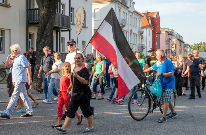 Menschen laufen mit einer Flagge des deutschen Reichs durch die Straßen