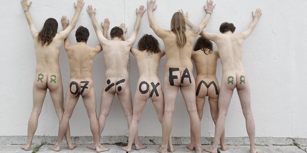 Sieben nackte Menschen stehen an einer weißen Wand, mit dem Rücken zum Betrachter. Auf ihren Hintern steht gemalt: 0,7% Oxfam