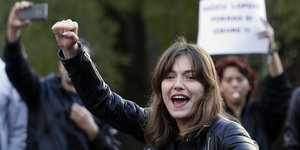Eine junge in einer Gruppe Demonstranten Frau ballt die rechte Hand zur Faust und ruft etwas.
