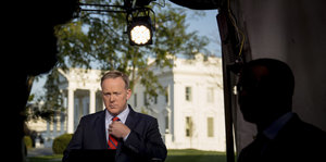 Sean Spicer steht im Schatten vor dem in der Sonne stahlenden weißen Haus
