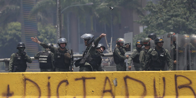 Schwer bewaffnete Polizisten stehen hinter einem gelben Banner, auf dem Dictadura steht