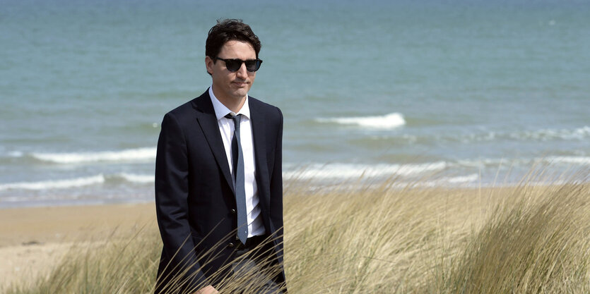 Justin Trudeau in schwarzem Anzug mit Sonnenbrille am Strand