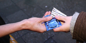 Zwei Hände, die eine reicht der anderen ein paar Kondome