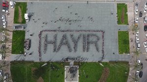 Aufsicht auf einen Platz, auf dem eine Gruppe von Menschen sich so zueinander gestellt hat, dass sie das Wort "Hayir" bildet.