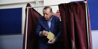 Präsident Erdogan kommt hinter dem Vorhang einer Wahlkabine hervor, mit dem Wahlzettel in der Hand