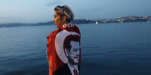 Eine Frau steht am Wasser. Sie hat eine Fahne um ihre Schultern gelegt, auf der das Konterfei Erdogans zu sehen ist