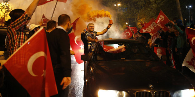 Menschen feiern auf der Straße. Sie schwenken türkische Fahnen und fahren im Autokorso