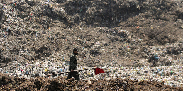 Ein Mann mit Mundschutz läuft auf einem Berg aus Müll