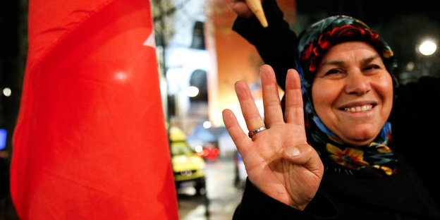 Eine Frau streckt vier Finger in die Höhe, eine Türkeiflagge neben sich