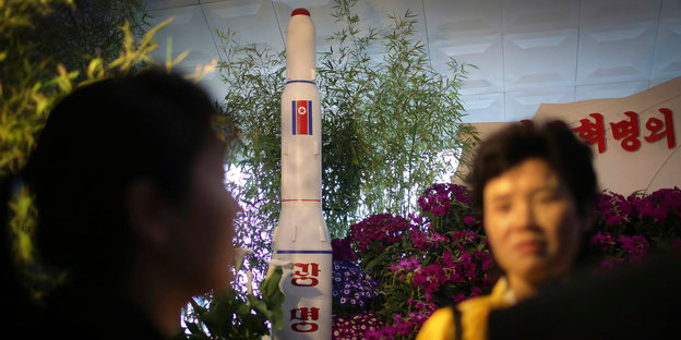 Ein Raketenmodell, zwei Frauen, viele Blumen