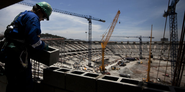 Ein Bauarbeiter legt einen Steinblock auf ein im Bau befindliches Stadion