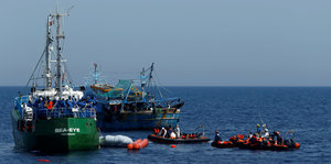 Ein grünes Fischkutter-ähnliches Schiff auf offener See, neben zwei Schlauchbooten und einem weiteren Fischkutter
