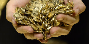 Zwei Hände halten einen großen Haufen Goldmünzen
