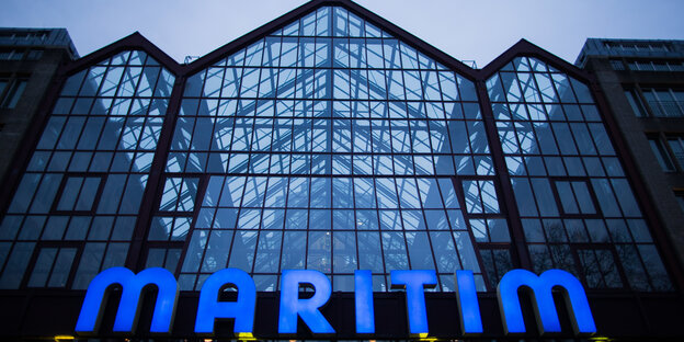 Ein gläsernes Haus von unten fotografiert, im unteren Teil des Bildes blaue Buchstaben, die das Wort Maritim formen