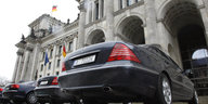 Mehrere schwarze Autos nebeneinander von unten fotografiert, im Hintergrund ein Bundestagsgebäude